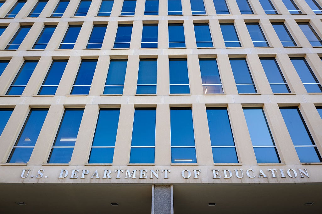 Image depicts the looming facade of the Department of Education headquarters in Washington DC. The name of the department is visible on the massive gray brutalist building.