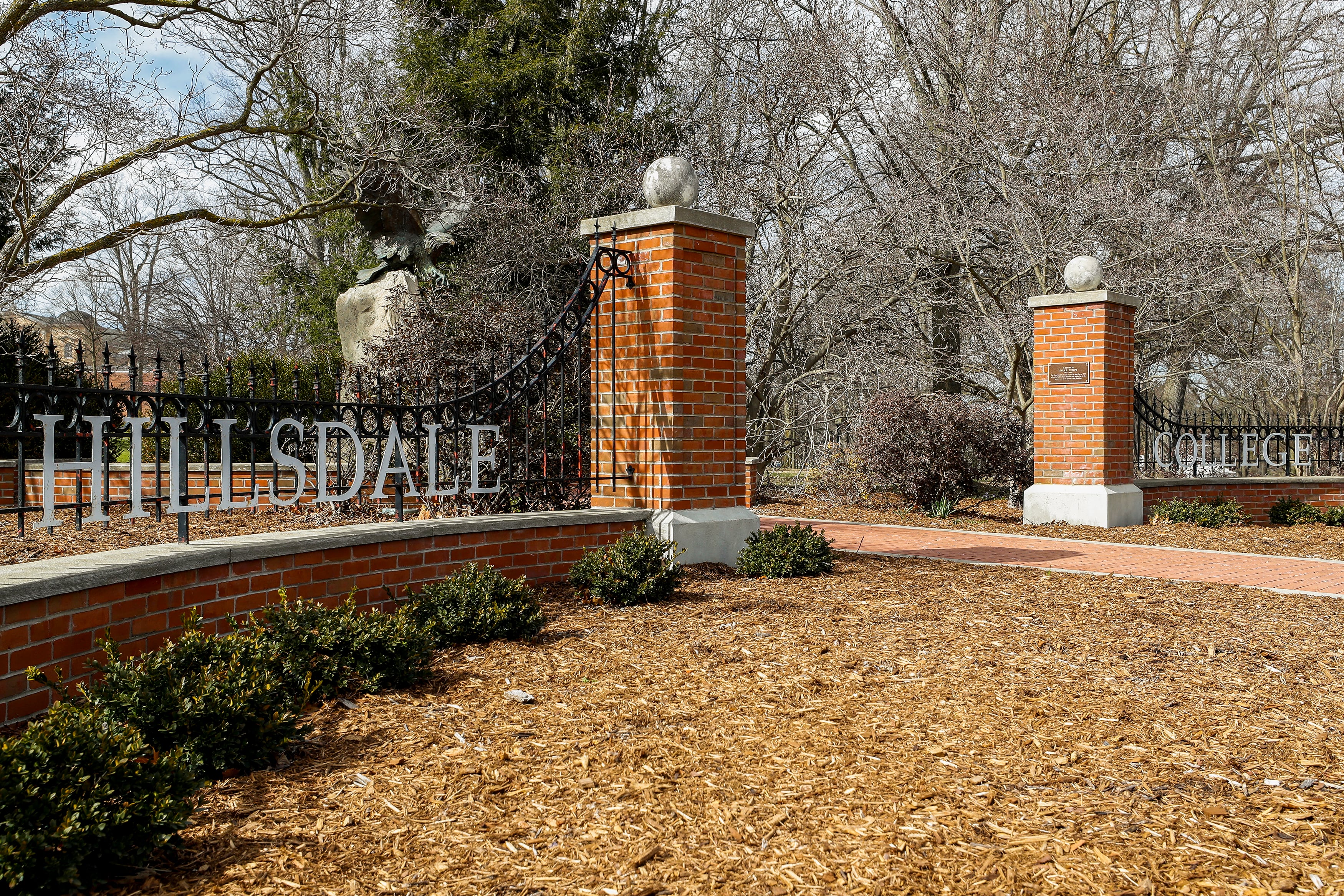 A brick entrance to a college campus outside with bare trees in the background.