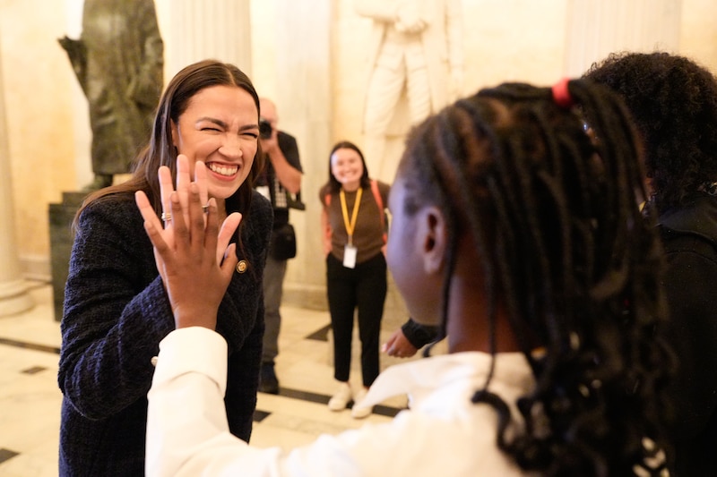A woman in a dark suit jacket smiles and high fives a student.