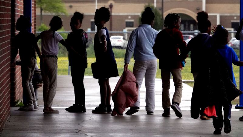 Young students line up outside of a school building.