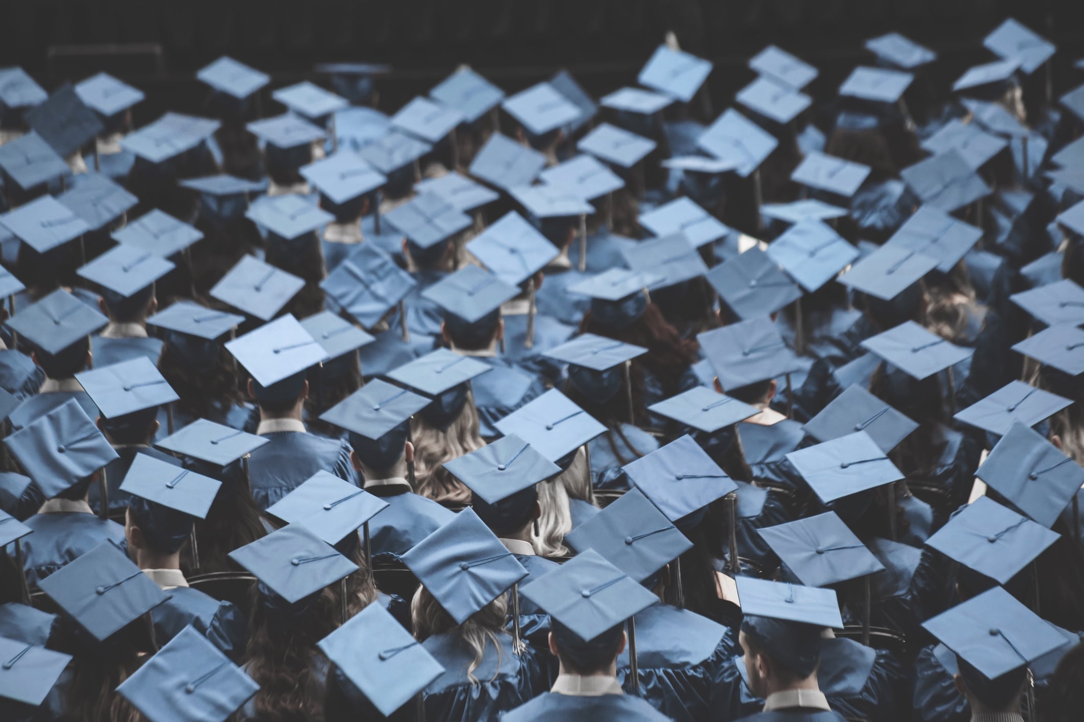 A large group of students wearing blue caps and gowns stand during their graduation ceremony.