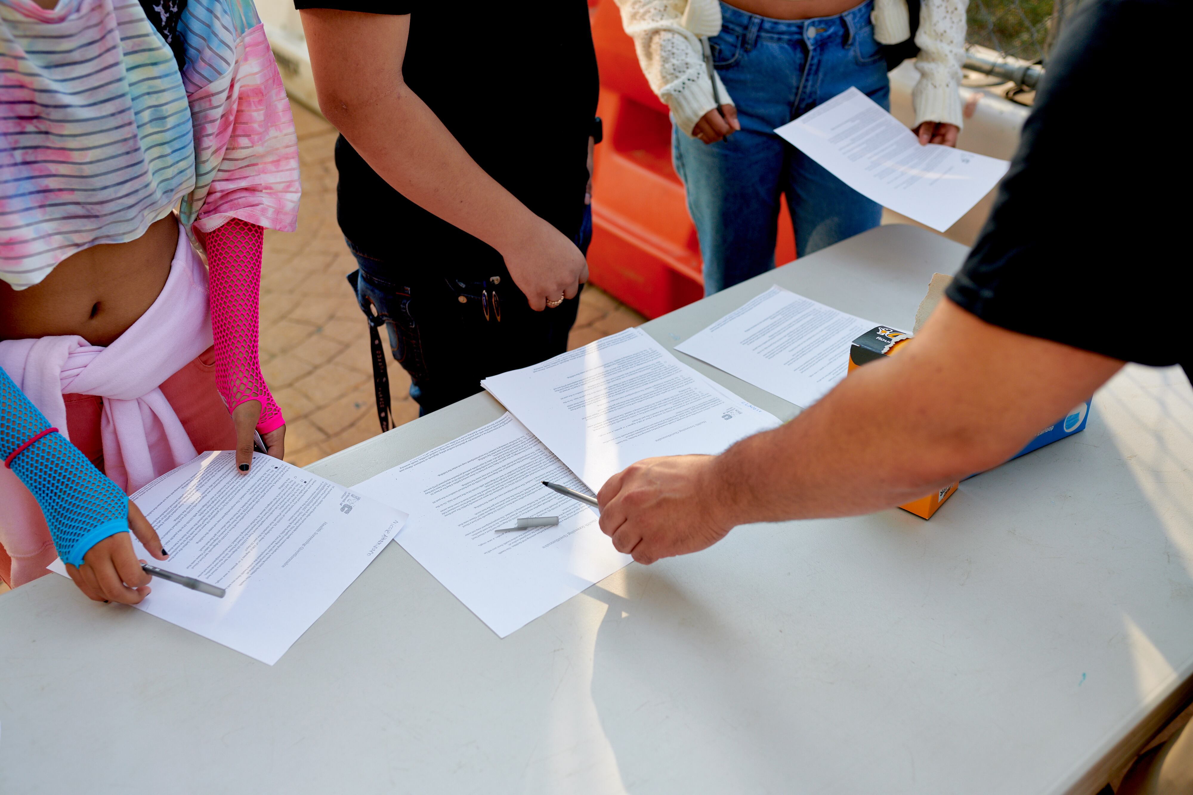 Students receive COVID screening forms and pens at a table from faculty.