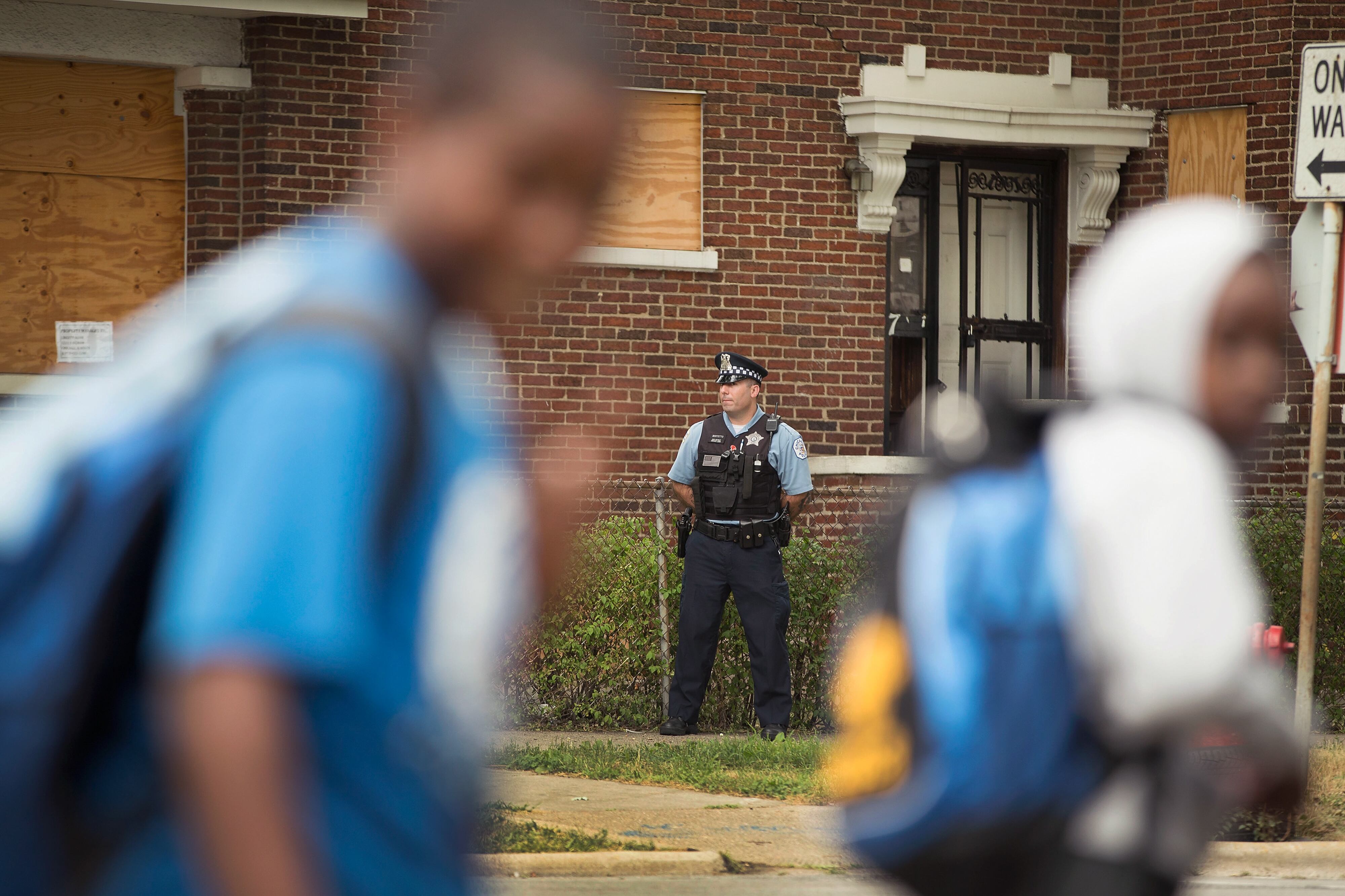 Children walk by a Chicago police officer, who is stationed in front of a brick building in the background.