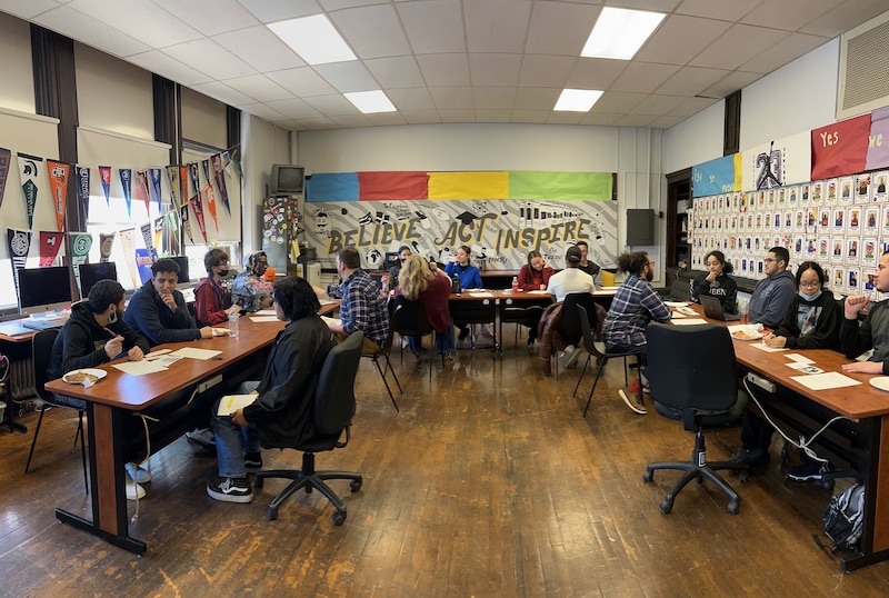 A photograph of a group of students at desks in a classroom.