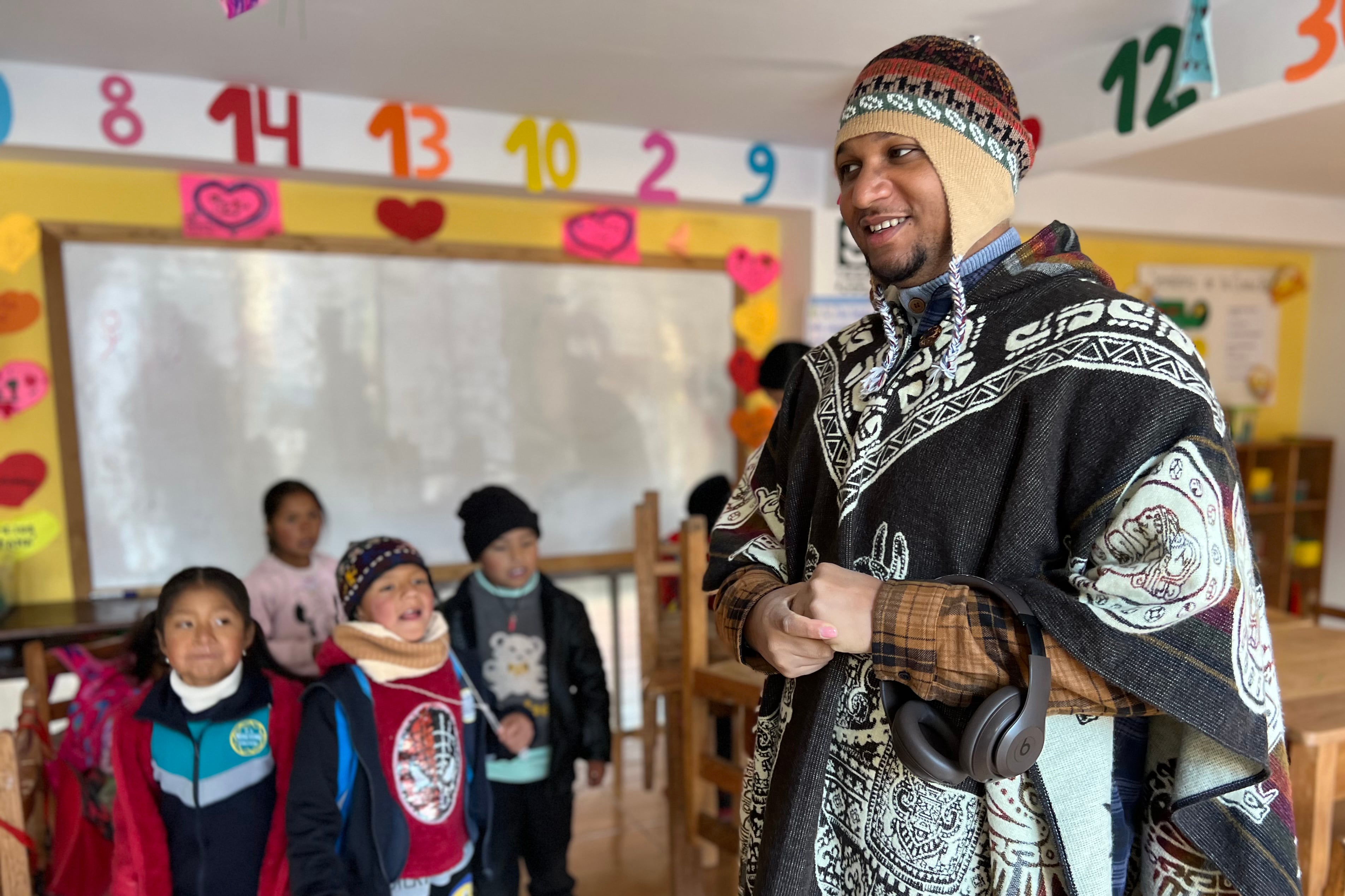 A man poses with a group of small children in front of a dry erase board in a classroom.