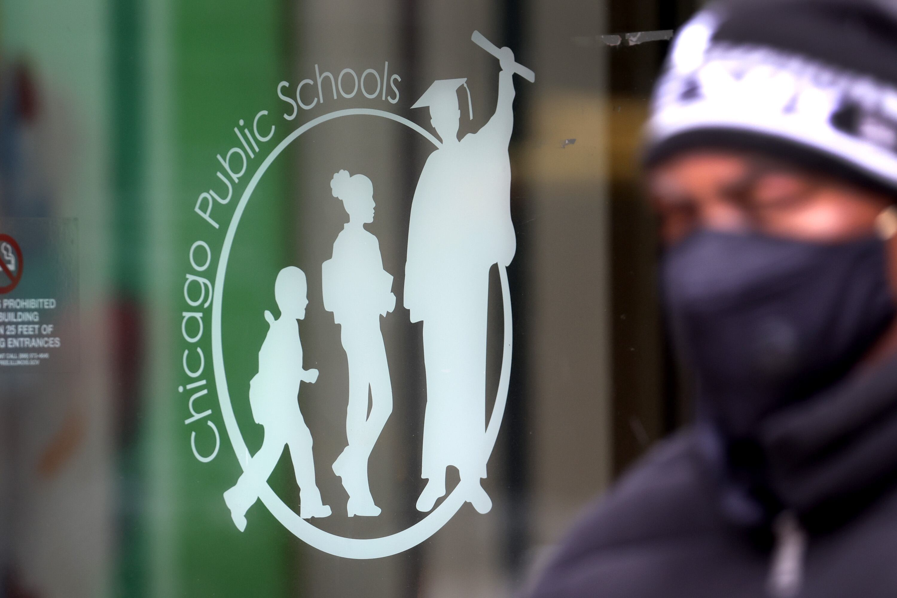 A man wearing a mask and knit cap walks past the Chicago Public Schools headquarters.