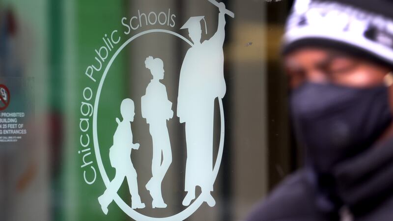 A man wearing a mask and knit cap walks past the Chicago Public Schools headquarters.