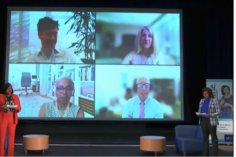 Two women, Chicago Public Schools top leaders Janice Jackson and  LaTanya McDade stand on stage flanking a large screen depicting four faces.