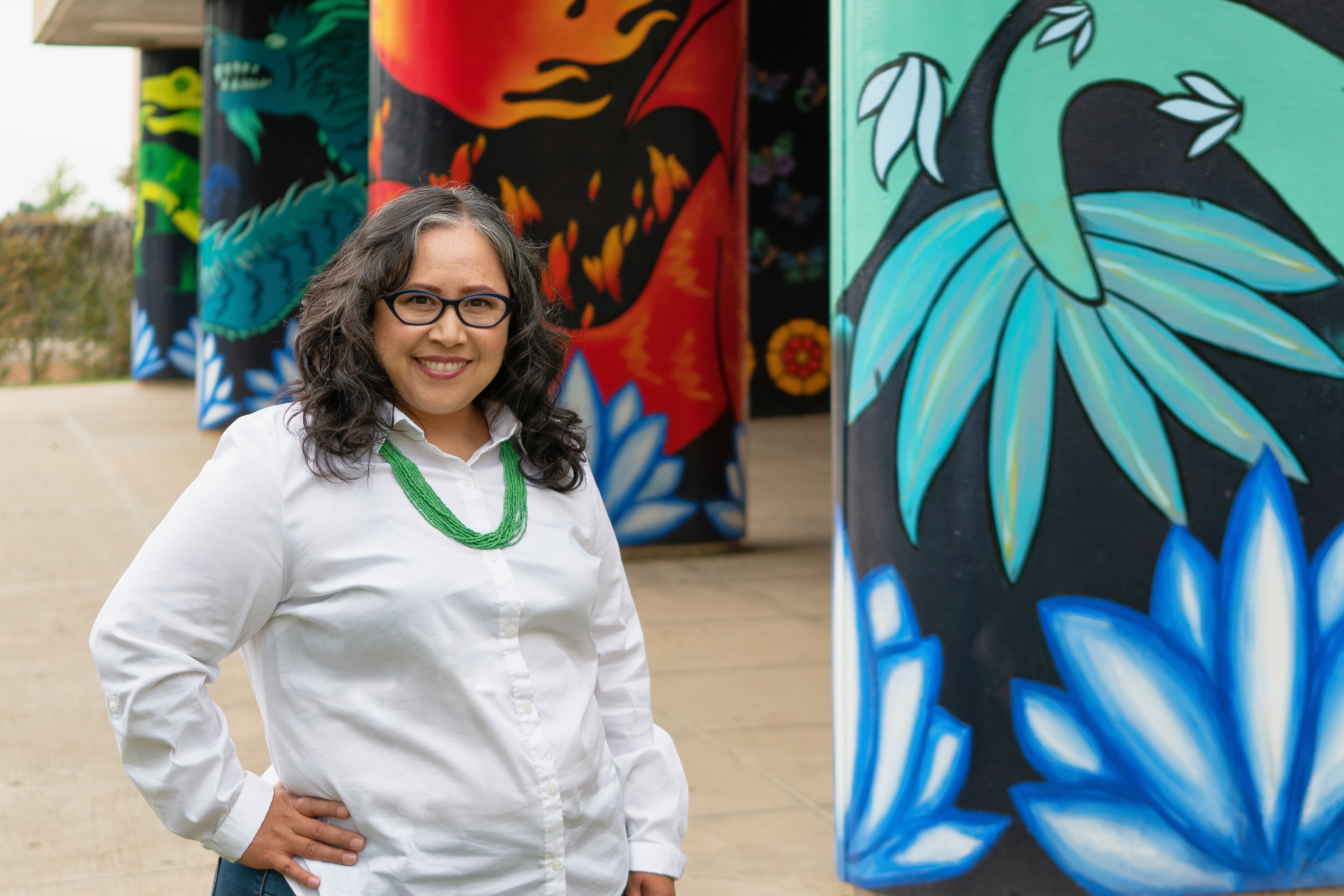 A woman wearing a white shirt and glasses poses for a portrait next to ornately painted pillars.