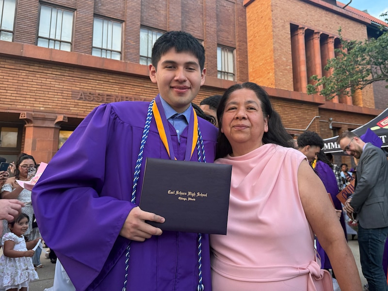 a photograph of a high school student wearing a graduation gown posing for a photograph with his mom.