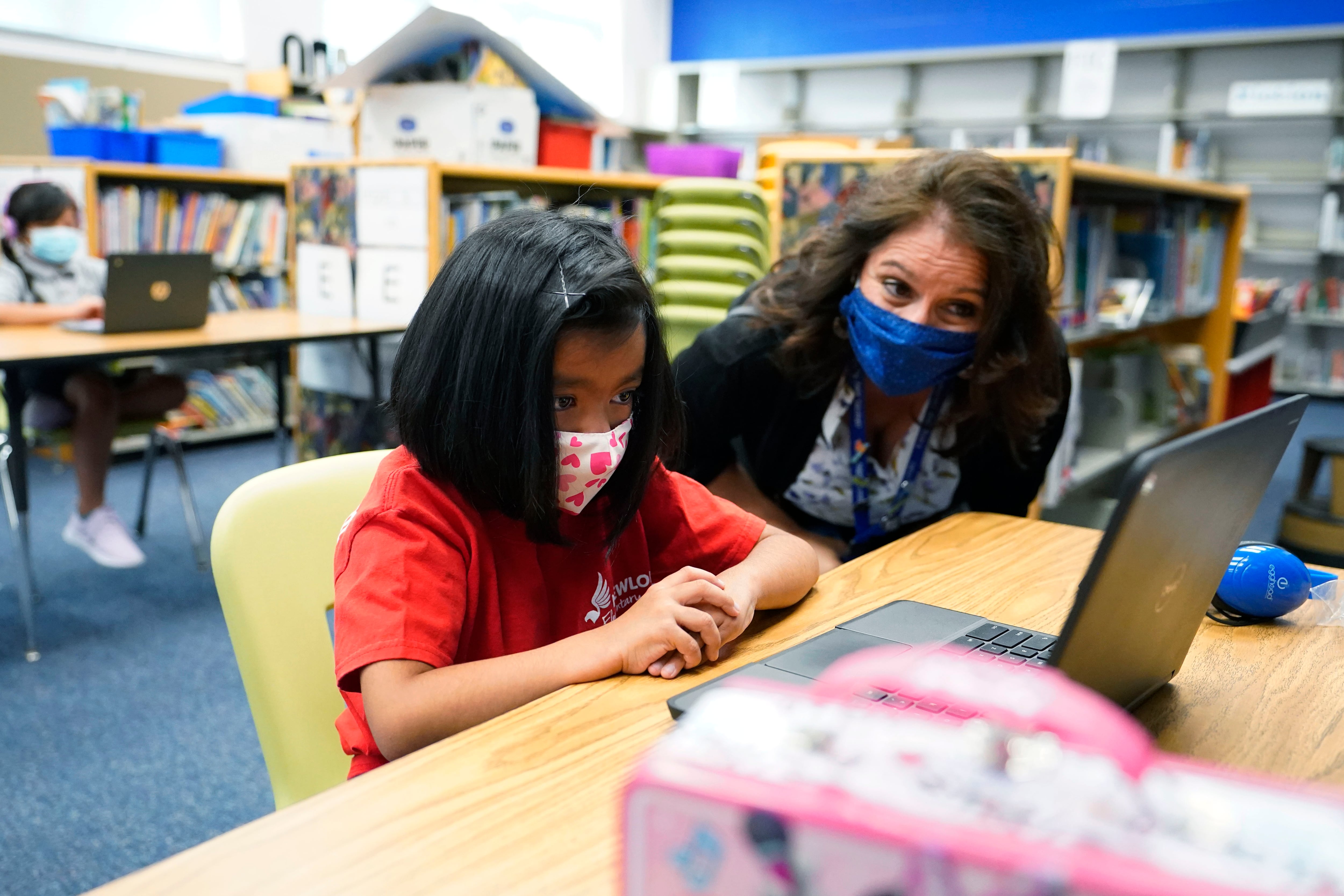 Denver Superintendent Susana Cordova talks to a masked girl working on a laptop at a learning center.