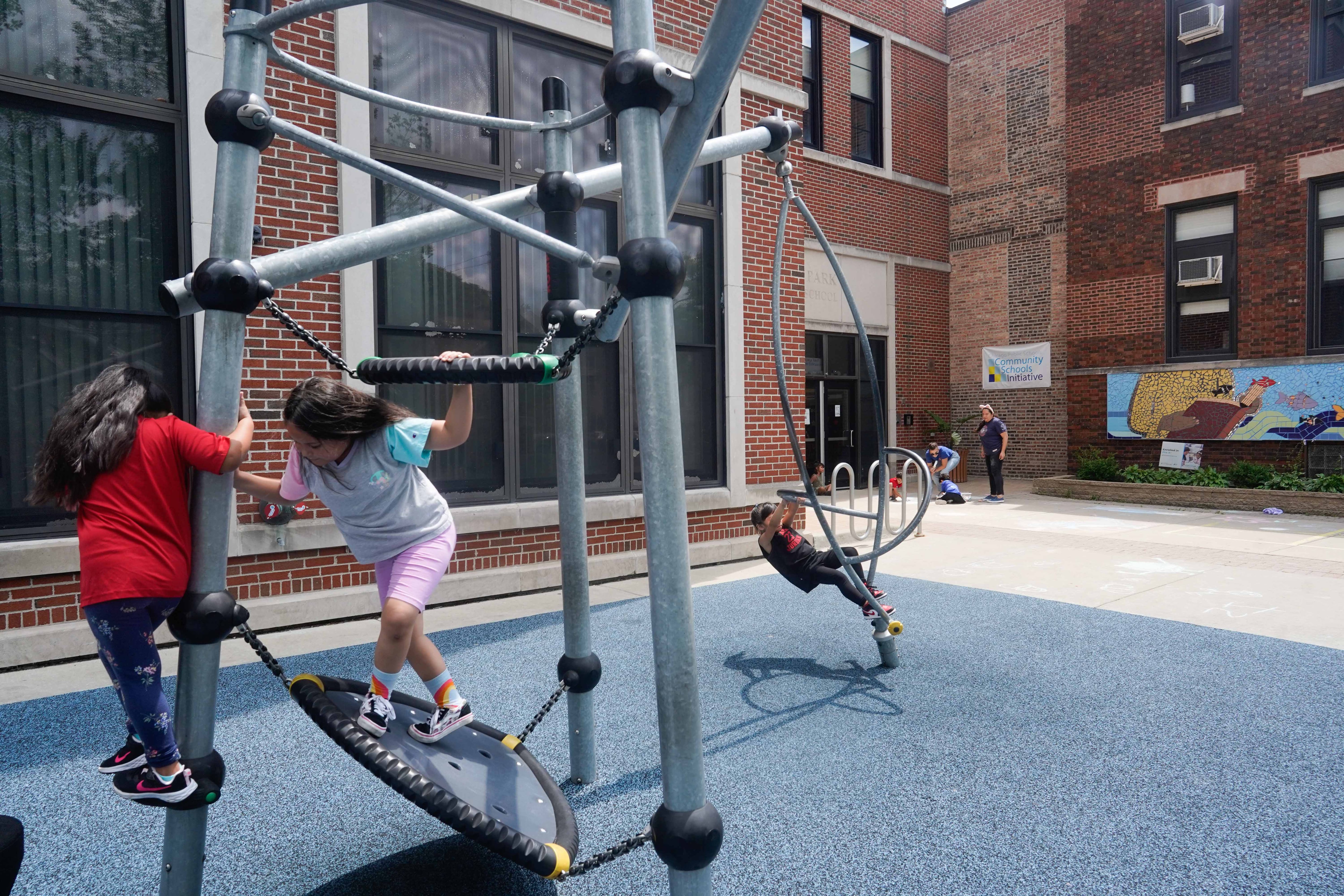 Three young children are playing together in a school playground during a sunny day.