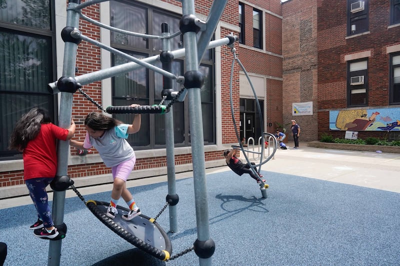 Three young children are playing together in a school playground during a sunny day.