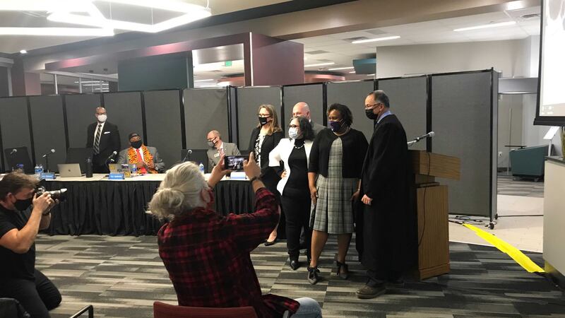 Denver school board members pose for a photo in front of a podium. People in the audience hold up cell phones to take photos.