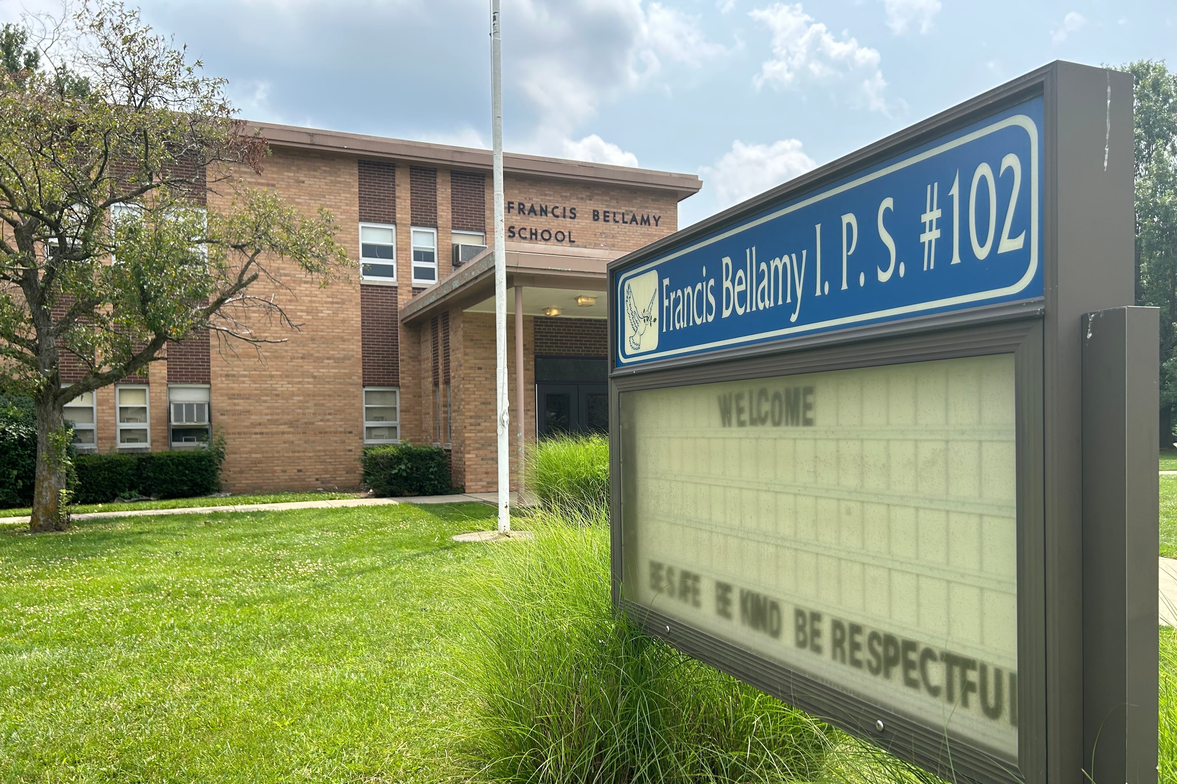 A close up of a school sign with a brick building in the background