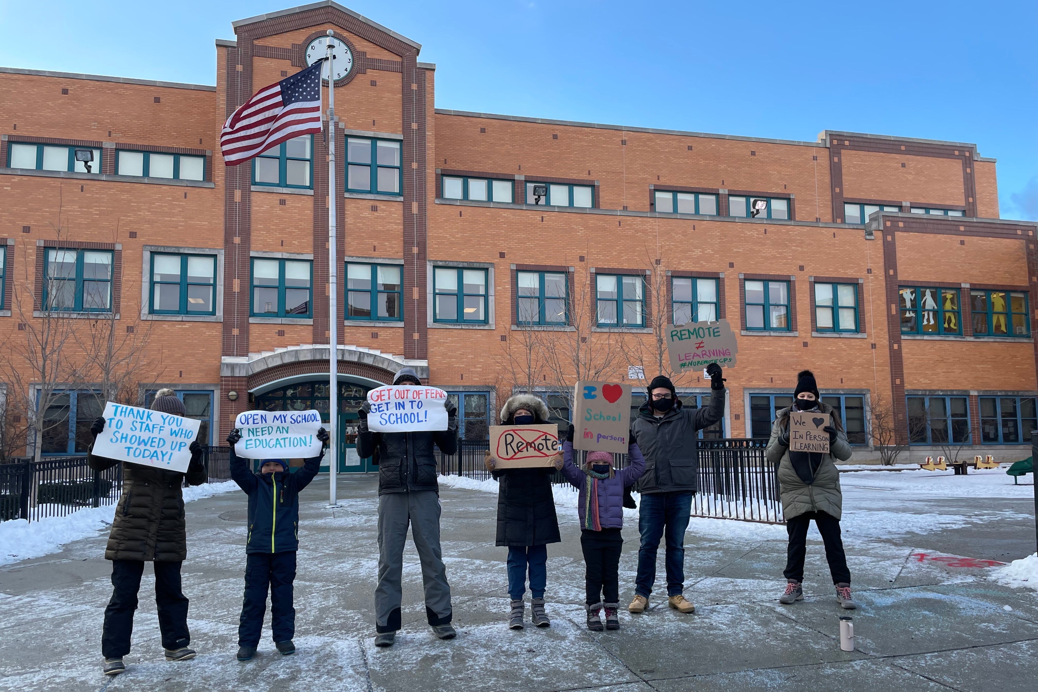 People dressed in winter coats hold signs in front of a school building in Chicago.