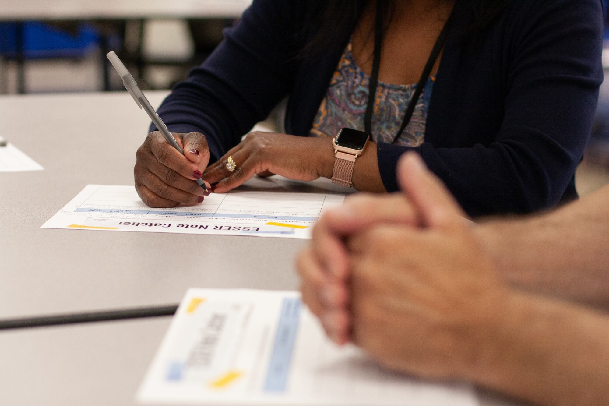 A person fills in a worksheet with a pen on a white table.