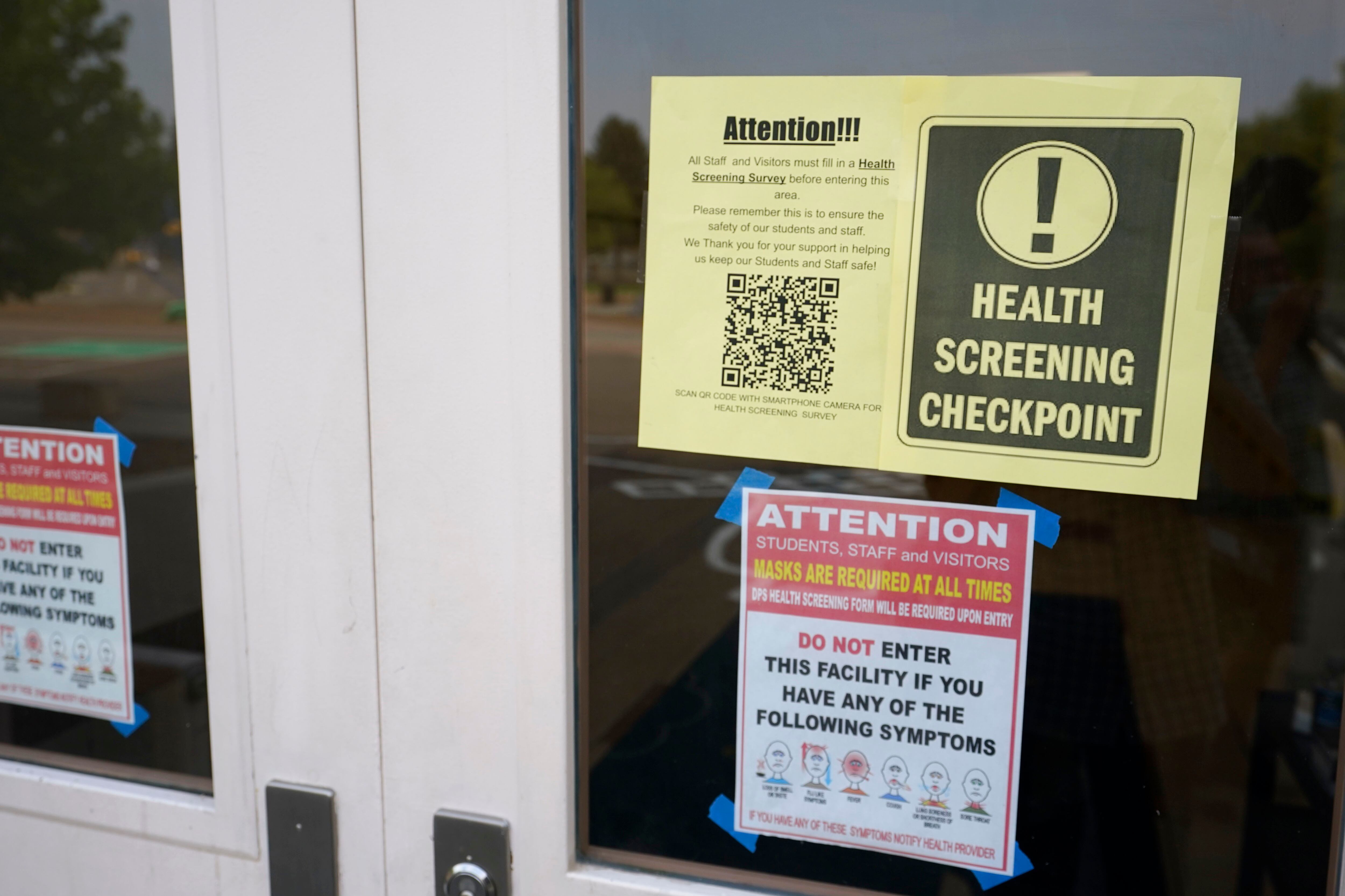 Sign for a health checkpoint hangs in the window of a schoolhouse door.