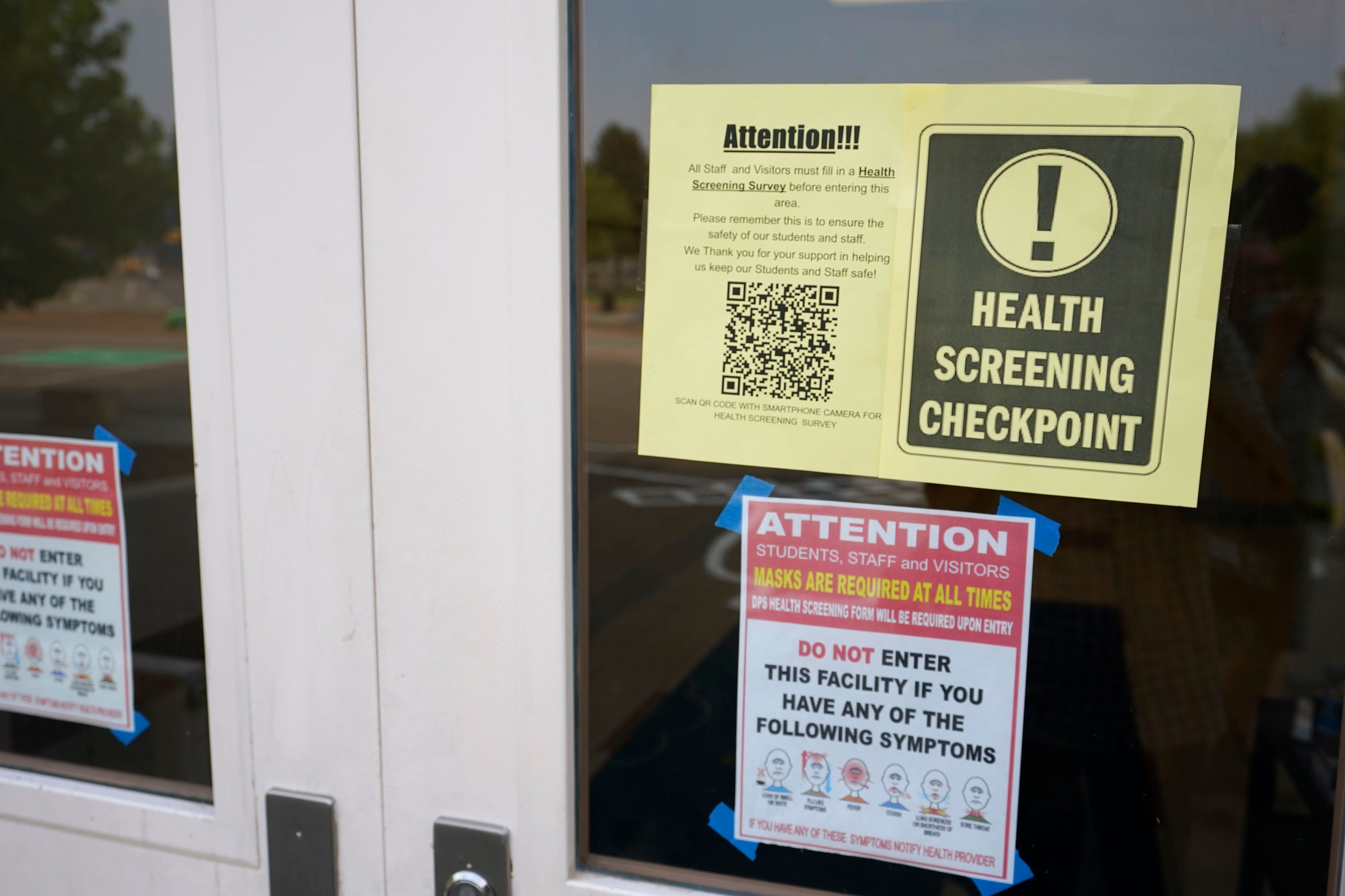 Sign for a health checkpoint hangs in the window of a schoolhouse door.