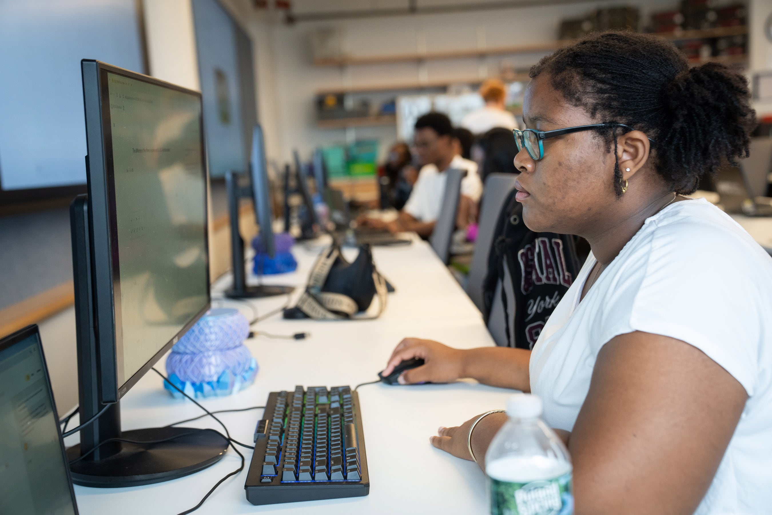 A female student with glasses and a white top works at a computer.