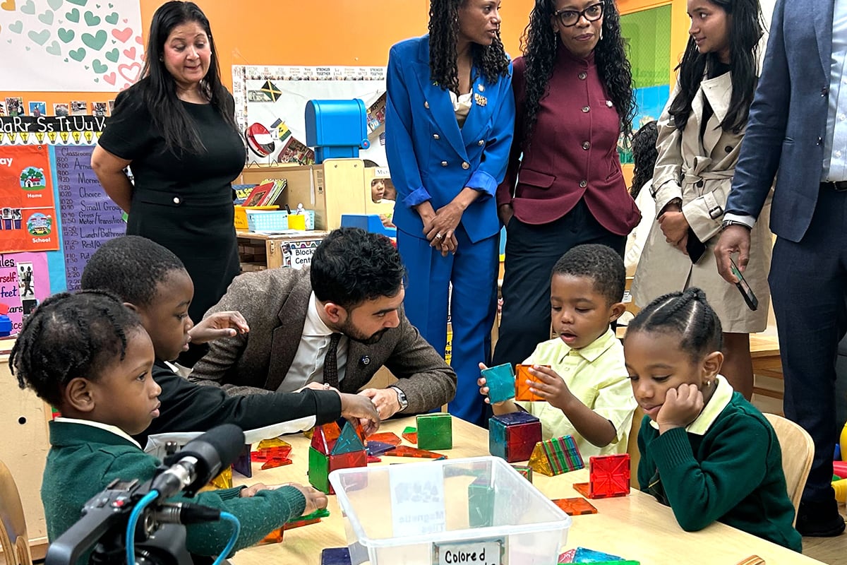 A man in a gray suit sits at a classroom table with some young children.