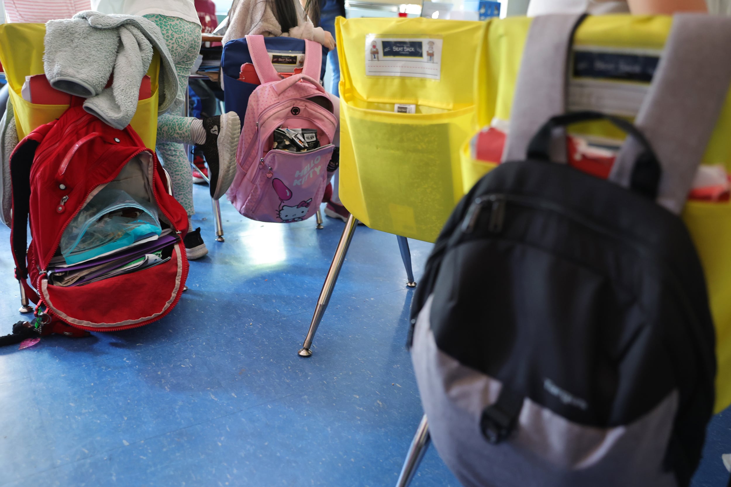 A photograph of young student chairs in a classroom with backpacks on the backs of the chairs.