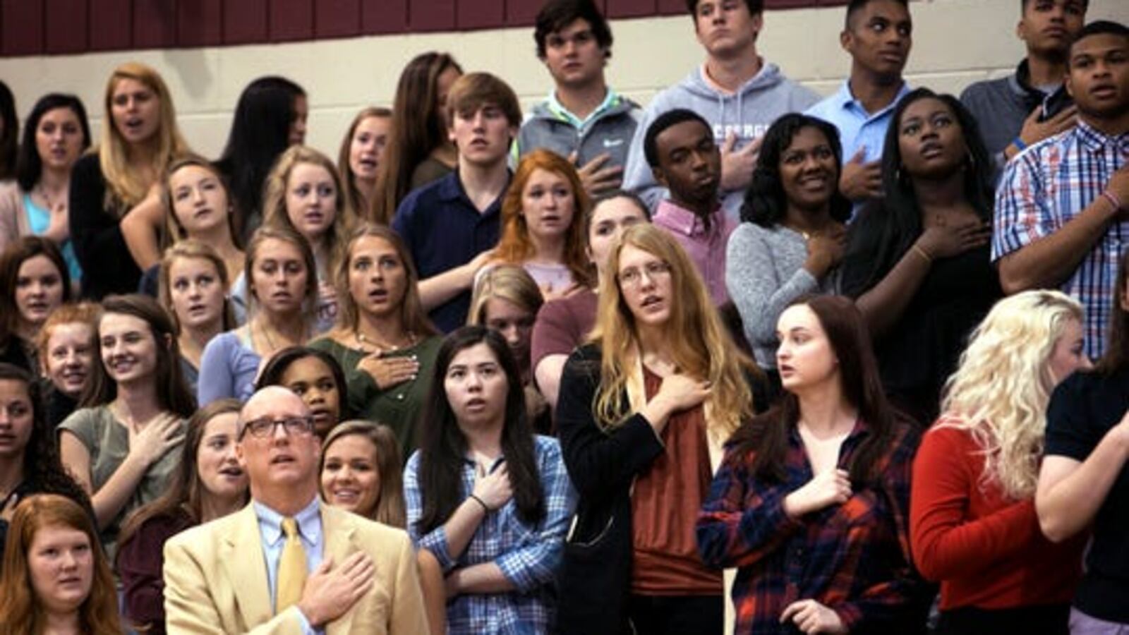 Students and an adult hold their hands over their hearts as they recite a pledge.