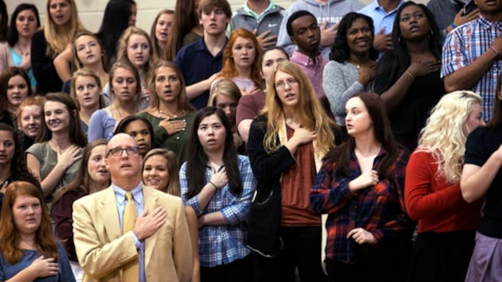 Students and an adult hold their hands over their hearts as they recite a pledge.