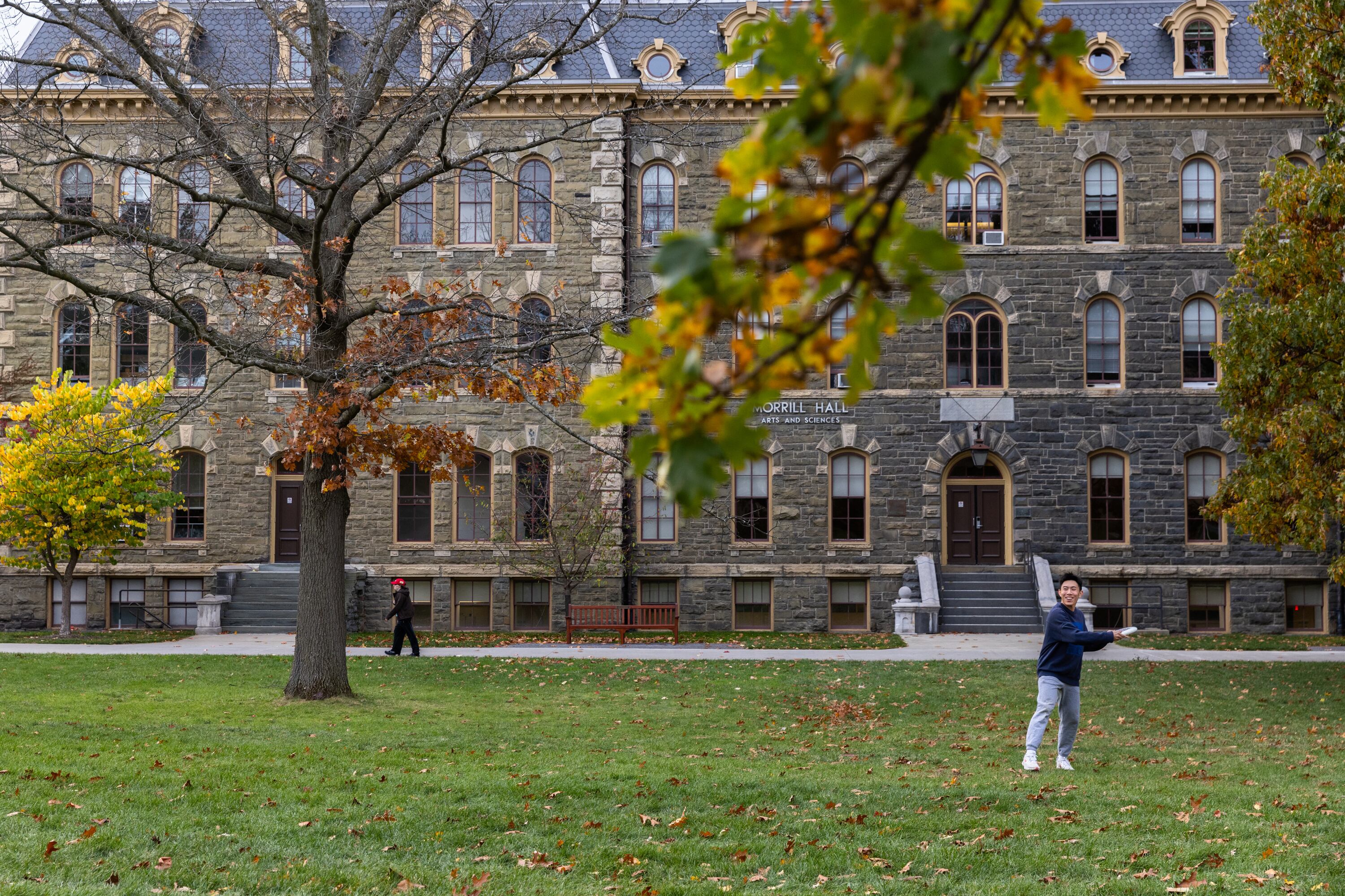 A student prepares to throw a frisbee while standing on a large green area in front of a large stone university building.