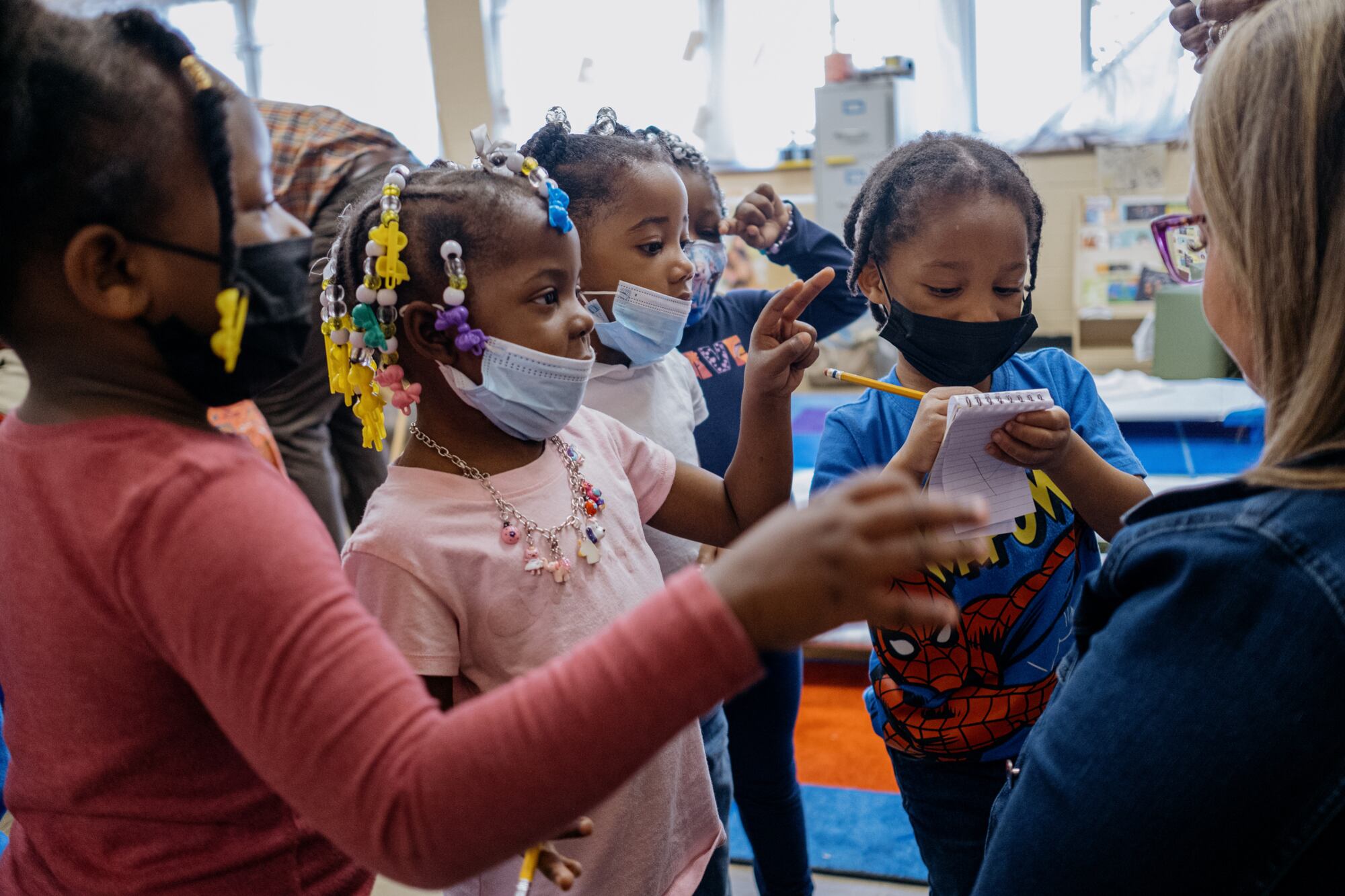 A group of preschool children gather around a teacher.