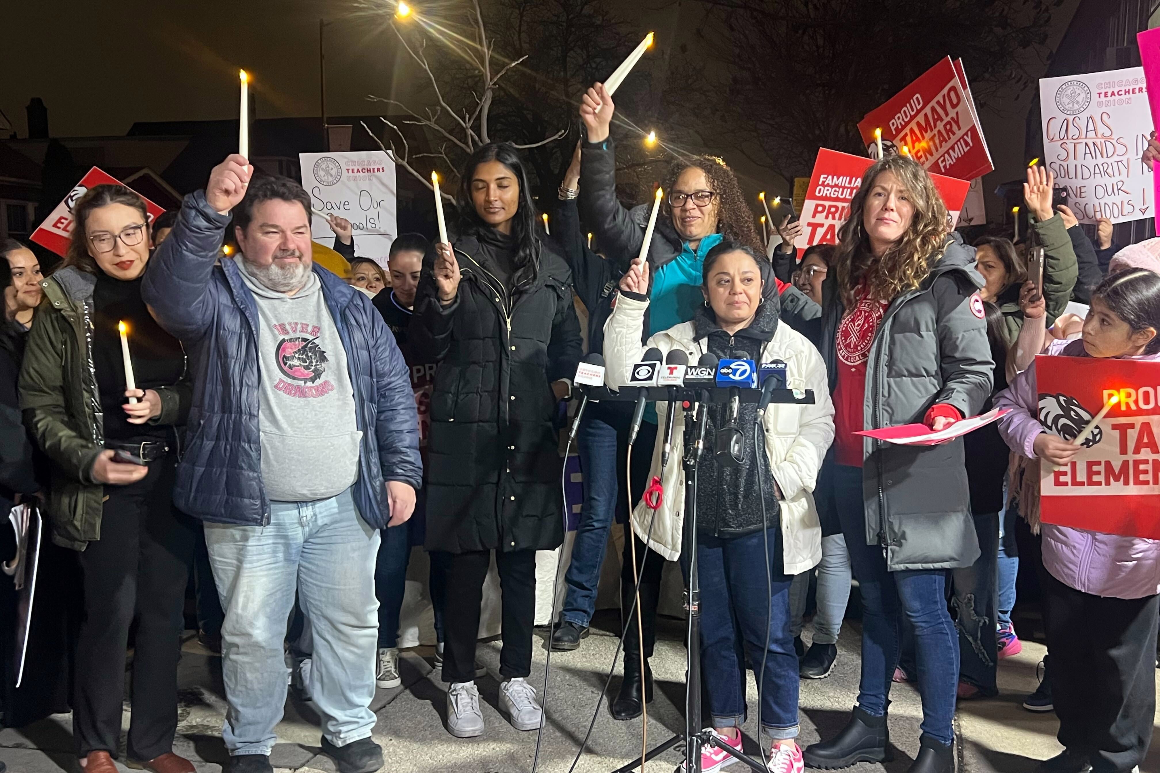 A group of people stand outside at night holding candles during a vigil.