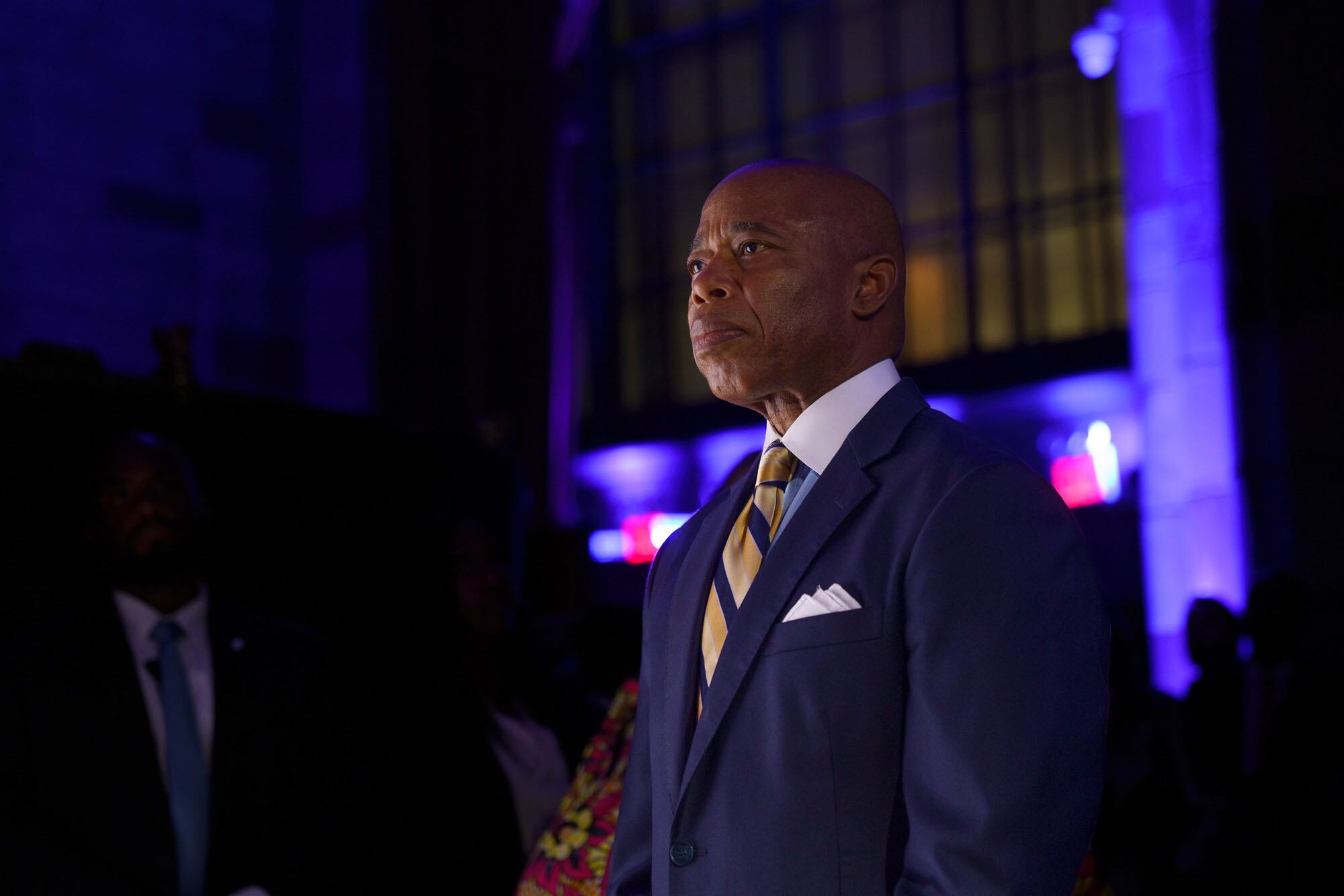 a man in a suit stands in a darkly lit area.