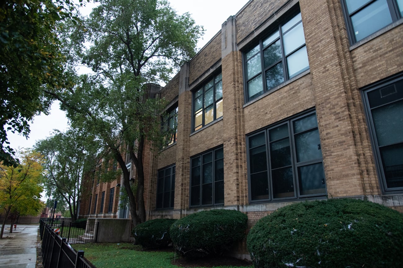 A photograph of the outside of a large stone building with green trees and bushes outside.
