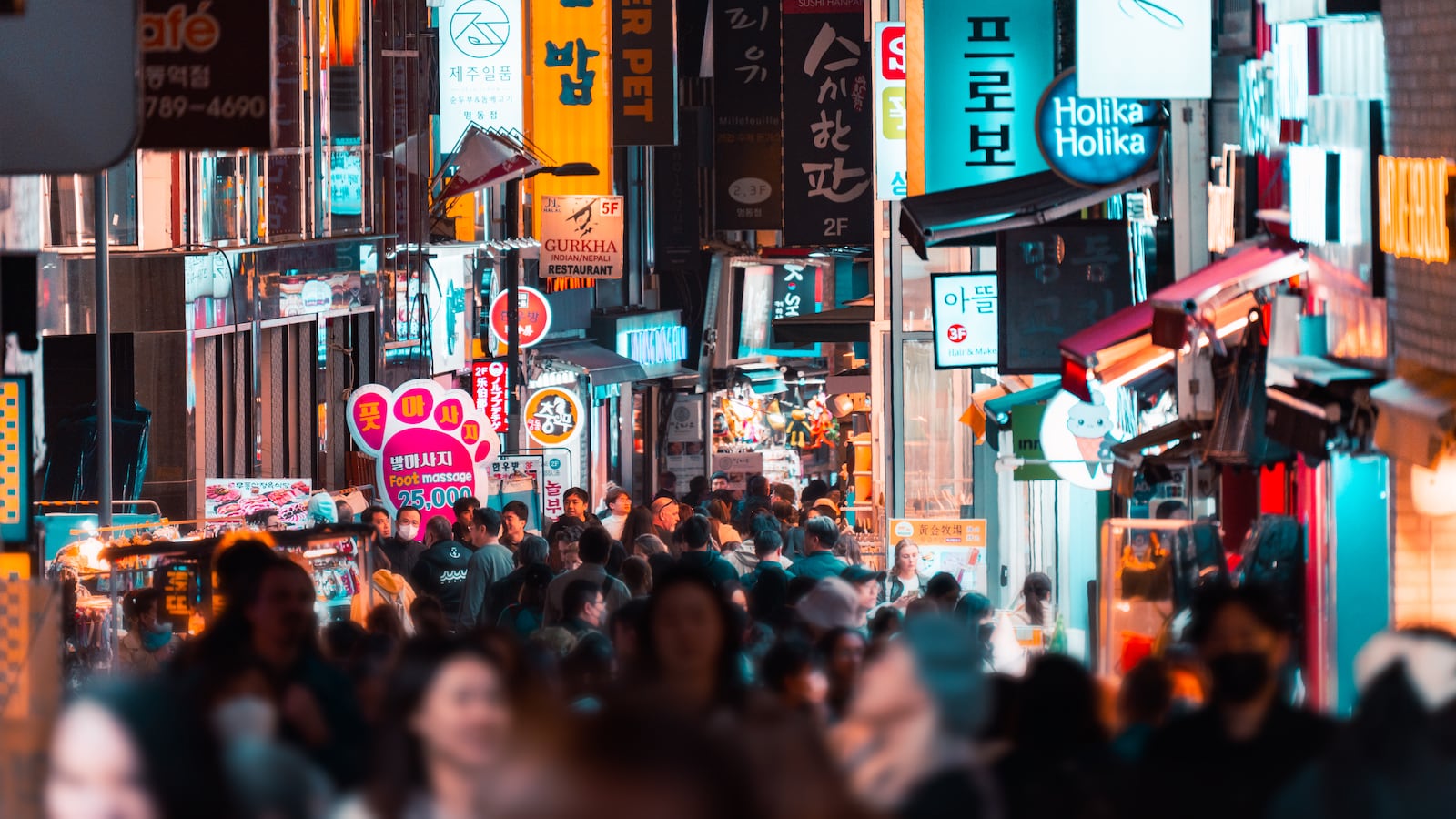 People walking among buildings with illuminated signs at night in Seoul, South Korea.