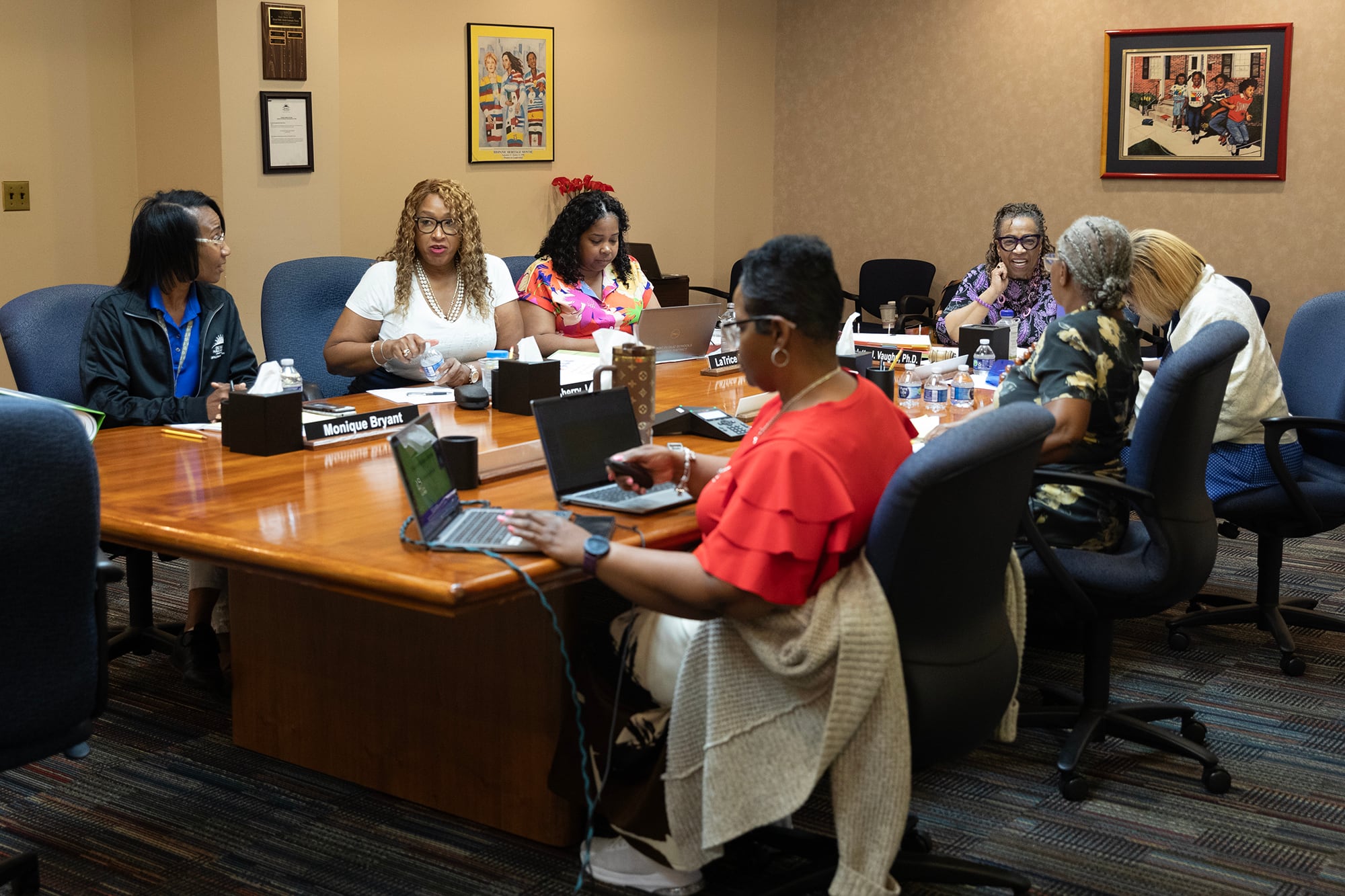 A room full of Black women in business clothes sit around a wooden table in a conference room.