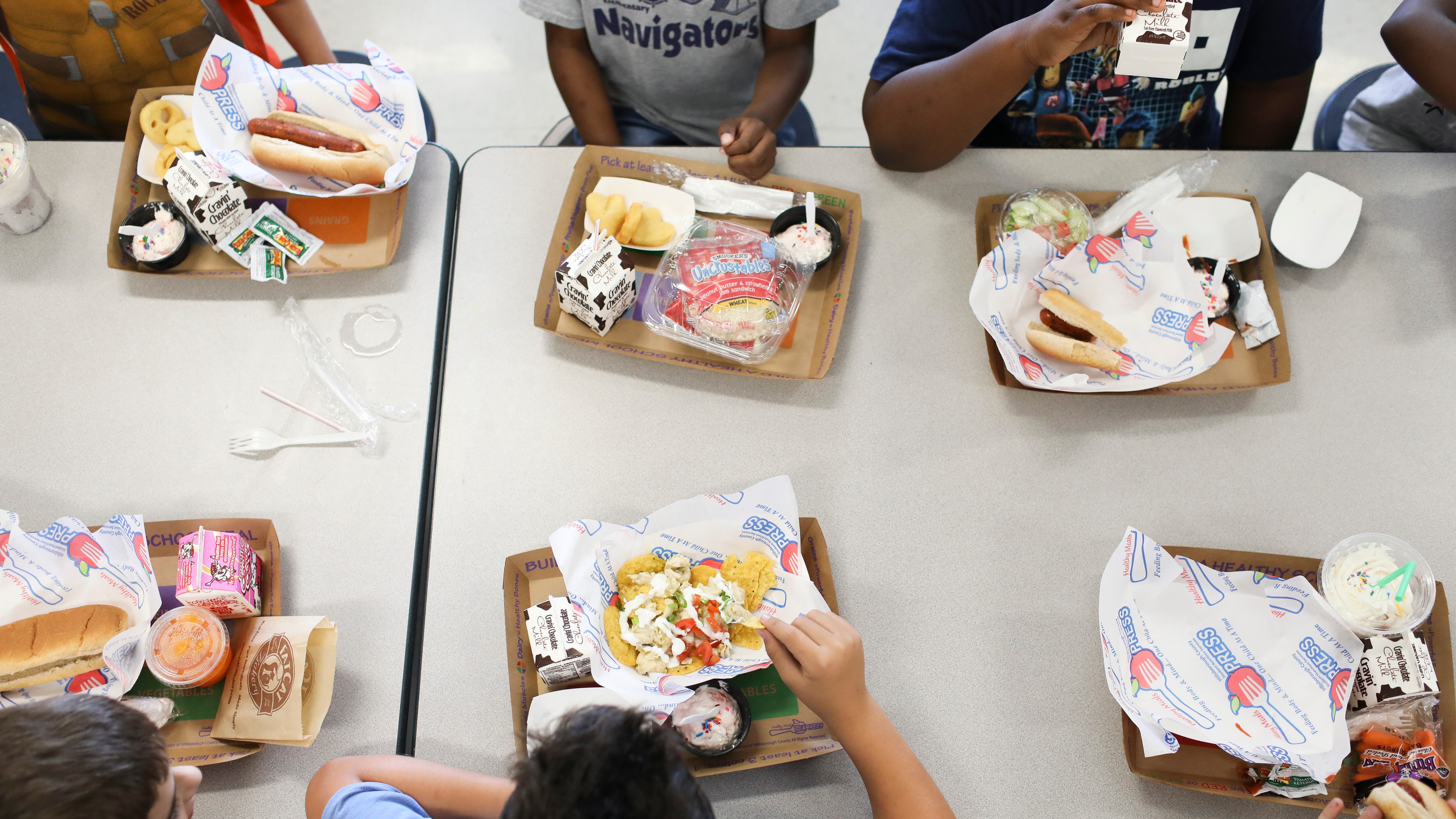 A group of children eat their school lunches at a table in the cafeteria.