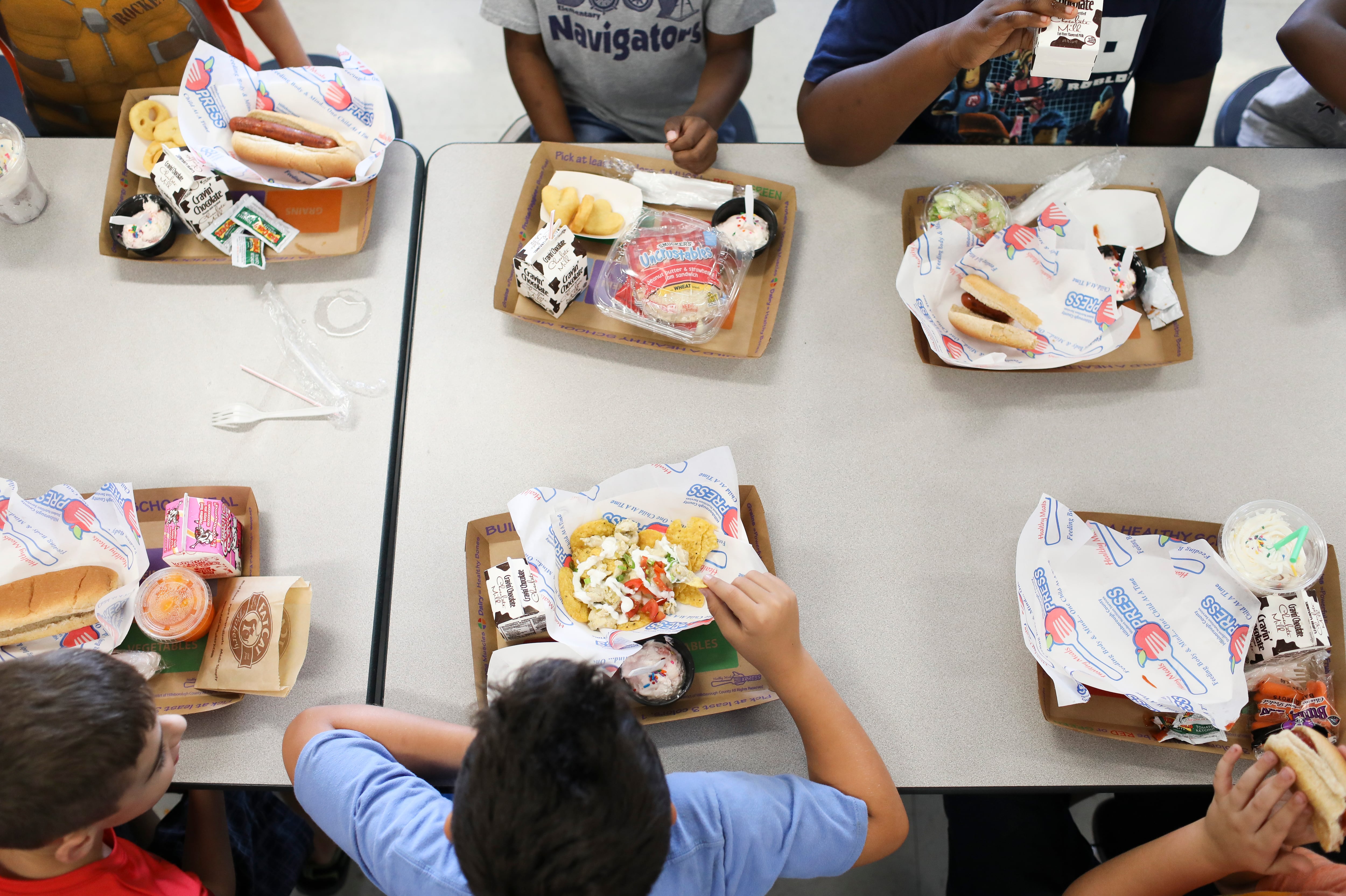 A group of children eat their school lunches at a table in the cafeteria.