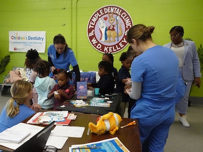 Four adults wearing scrubs give out stickers to a large group of young students in the dental office.