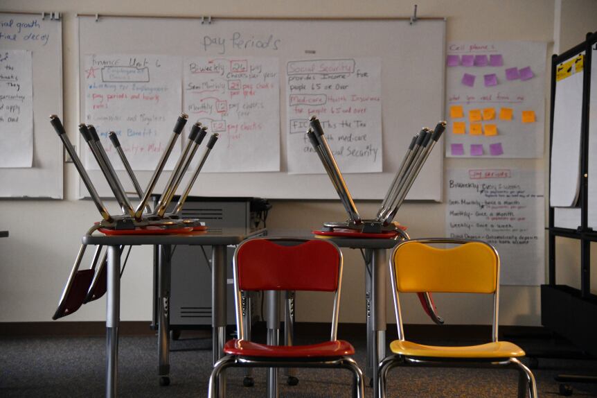 Chairs upside-down on a table and two empty chairs sit in an empty classroom.