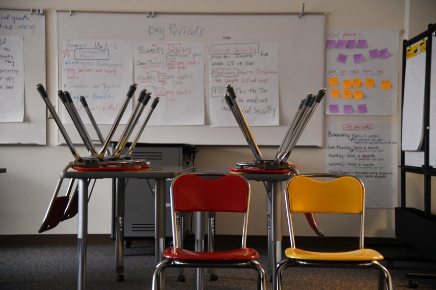 Chairs upside-down on a table and two empty chairs sit in an empty classroom.