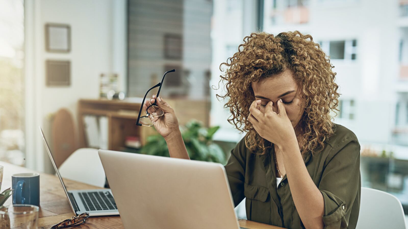 A stressed out teacher sitting at her laptop rubs her eyes.