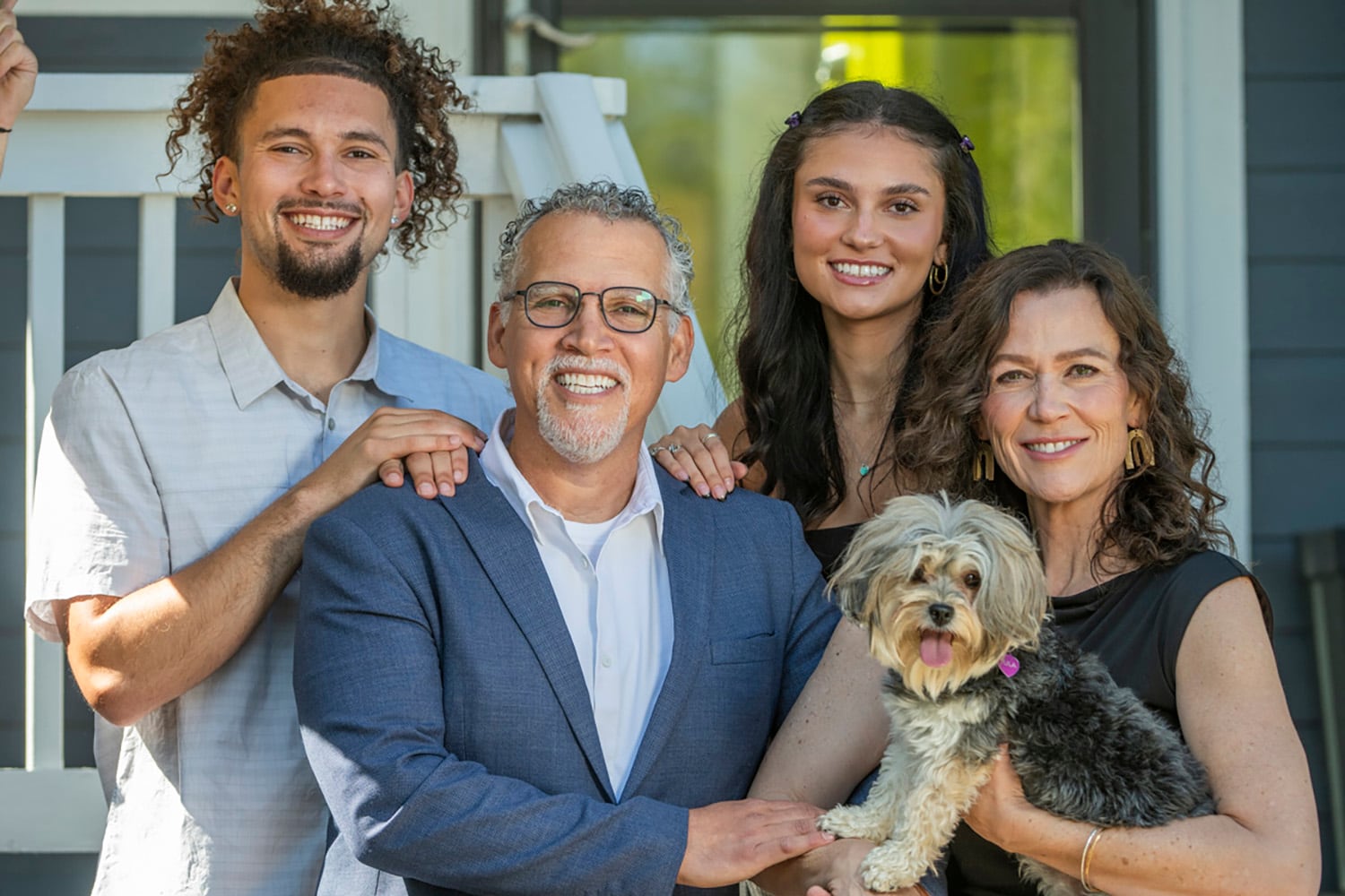 A family of four, hold a dog and pose for a photograph.
