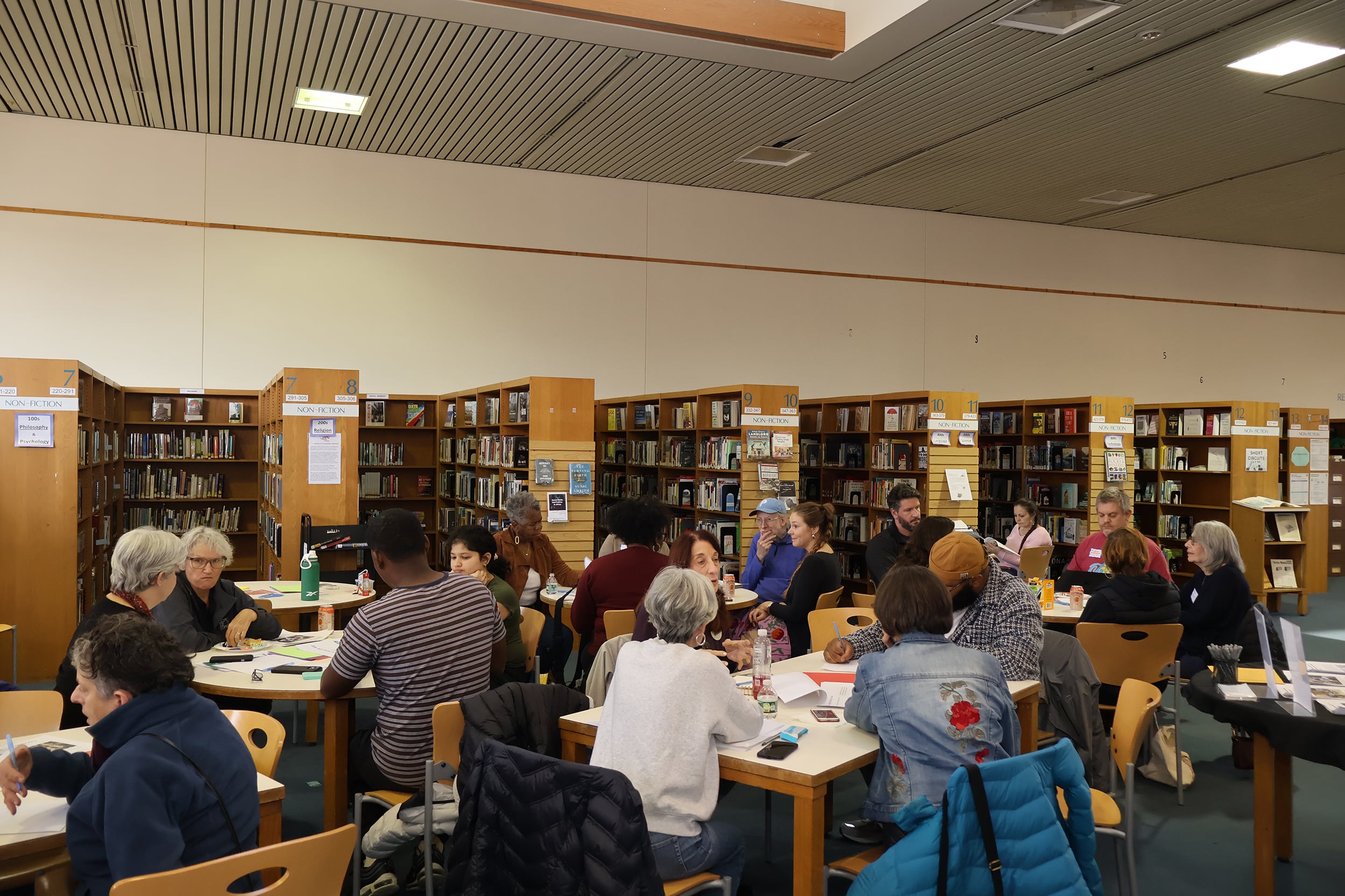 A photograph of a group of adults sitting in a school library.