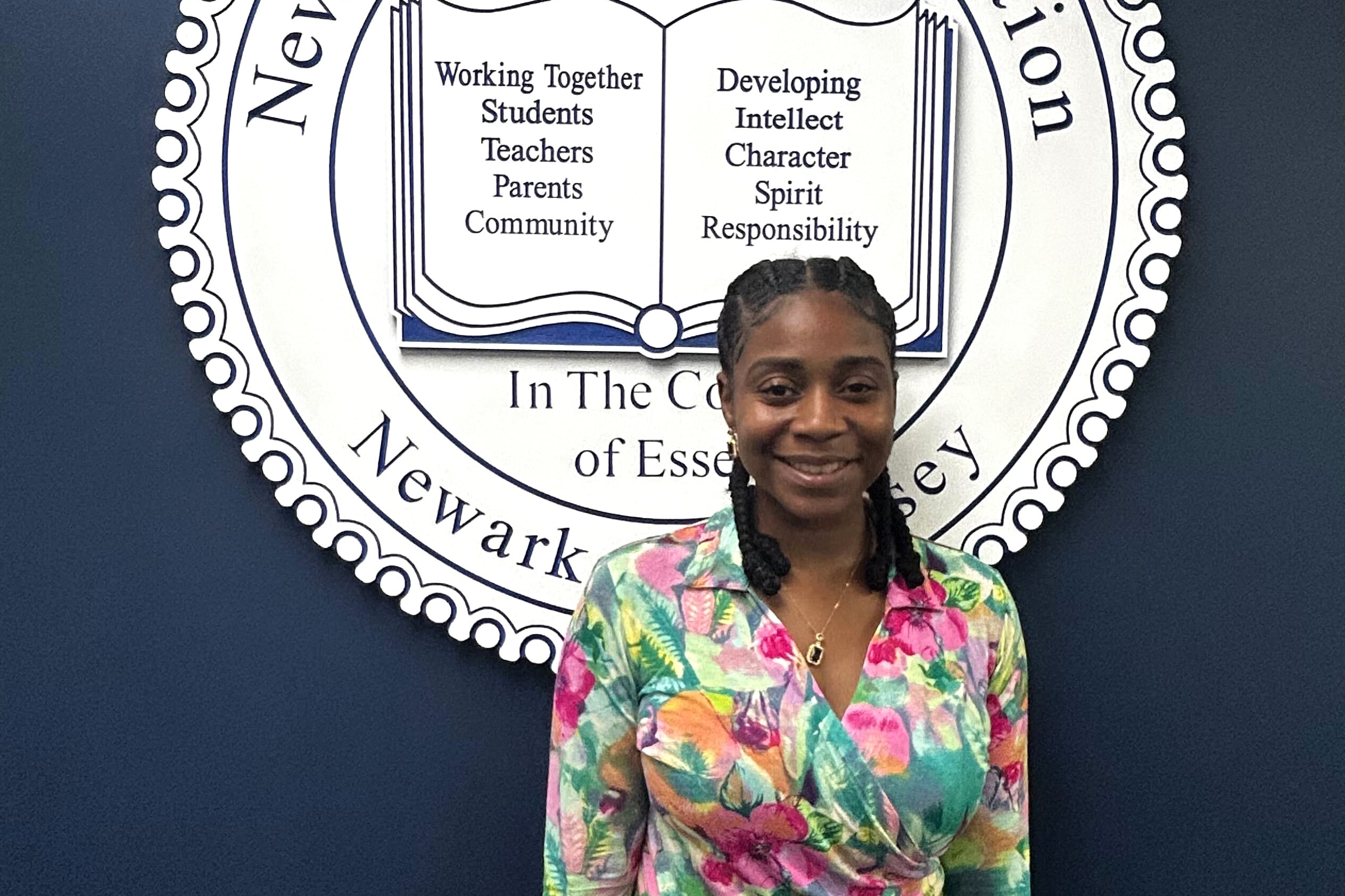 A woman in a brightly colored blouse stands in front of an official seal.