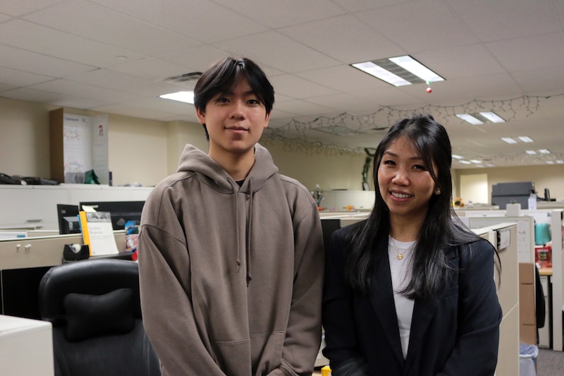 One student and one adult stand next to each other posing for a photograph in a classroom.