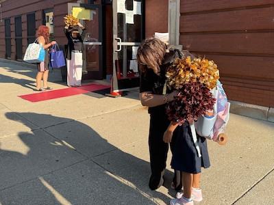 A photograph of adults and students greeting each other outside of a brick school building.