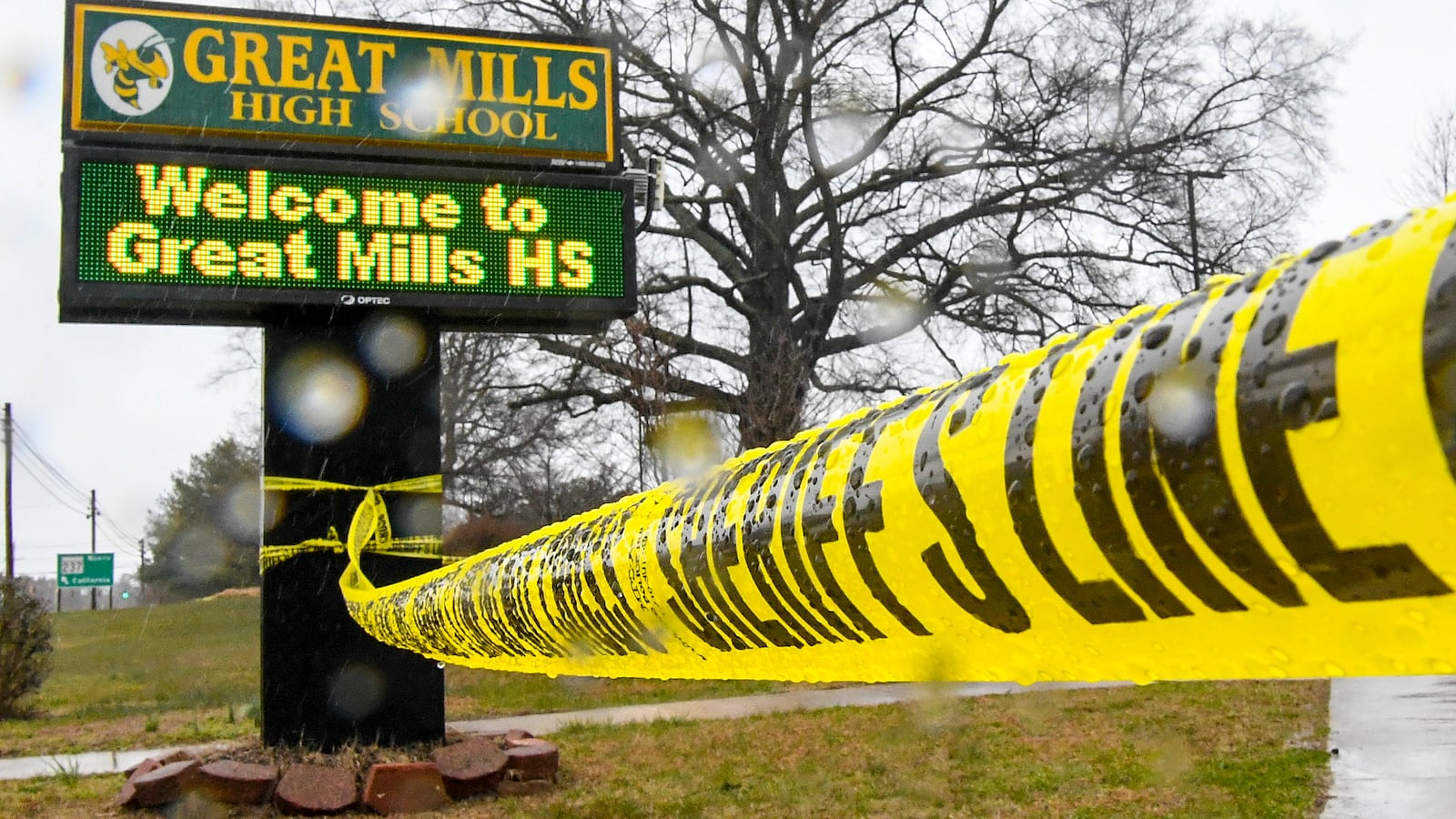 A green and yellow sign that says Great Mills High School. Near it is yellow police tape.