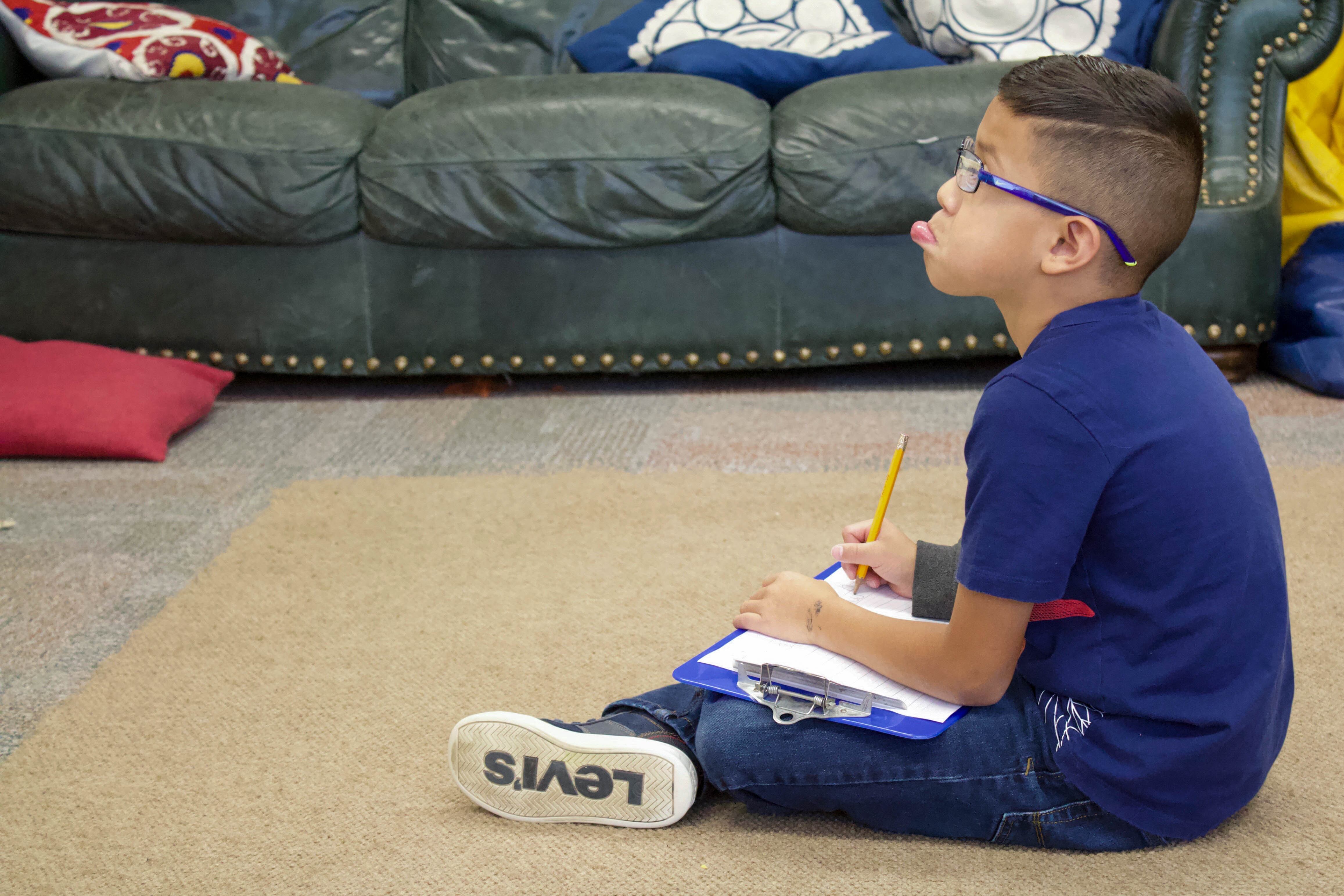 A Lake County elementary school student works on an assignment away from his desk. (Photo by Nic Garcia/Chalkbeat)