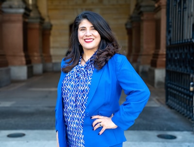 A woman with dark hair stands in a blue suit jacket and blouse