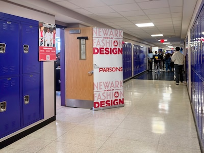 A high school hallway with posters on the wall and people walking in the background.